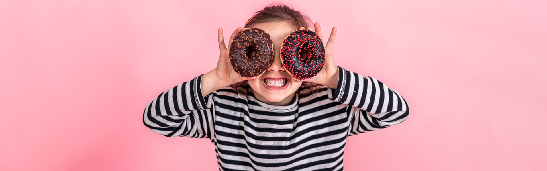 pediatric dentist patient model holding up two donuts in front of their eyes and looking through the donut holes