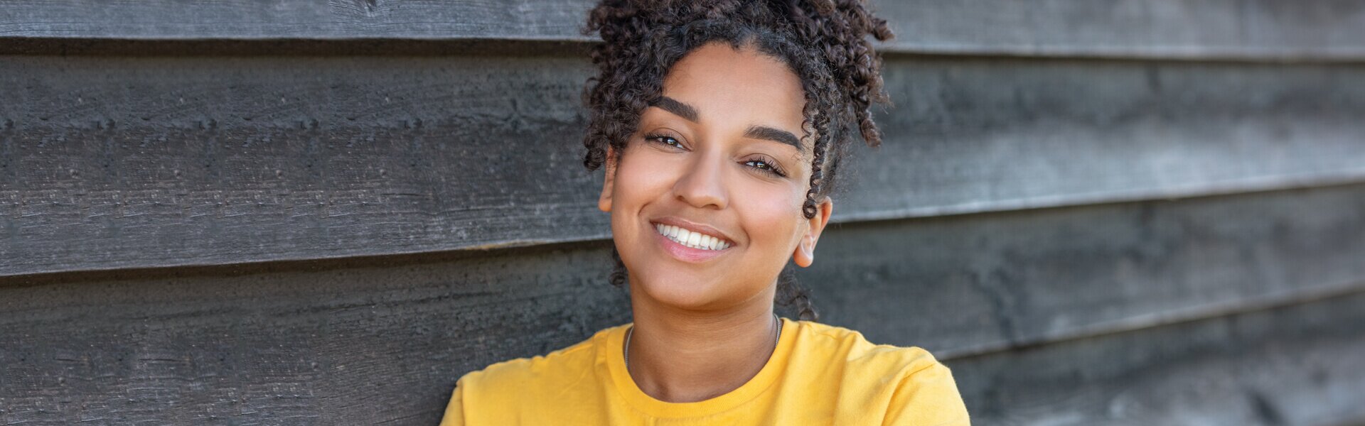 dentist patient model in a yellow sweater smiling and leaning against a barn